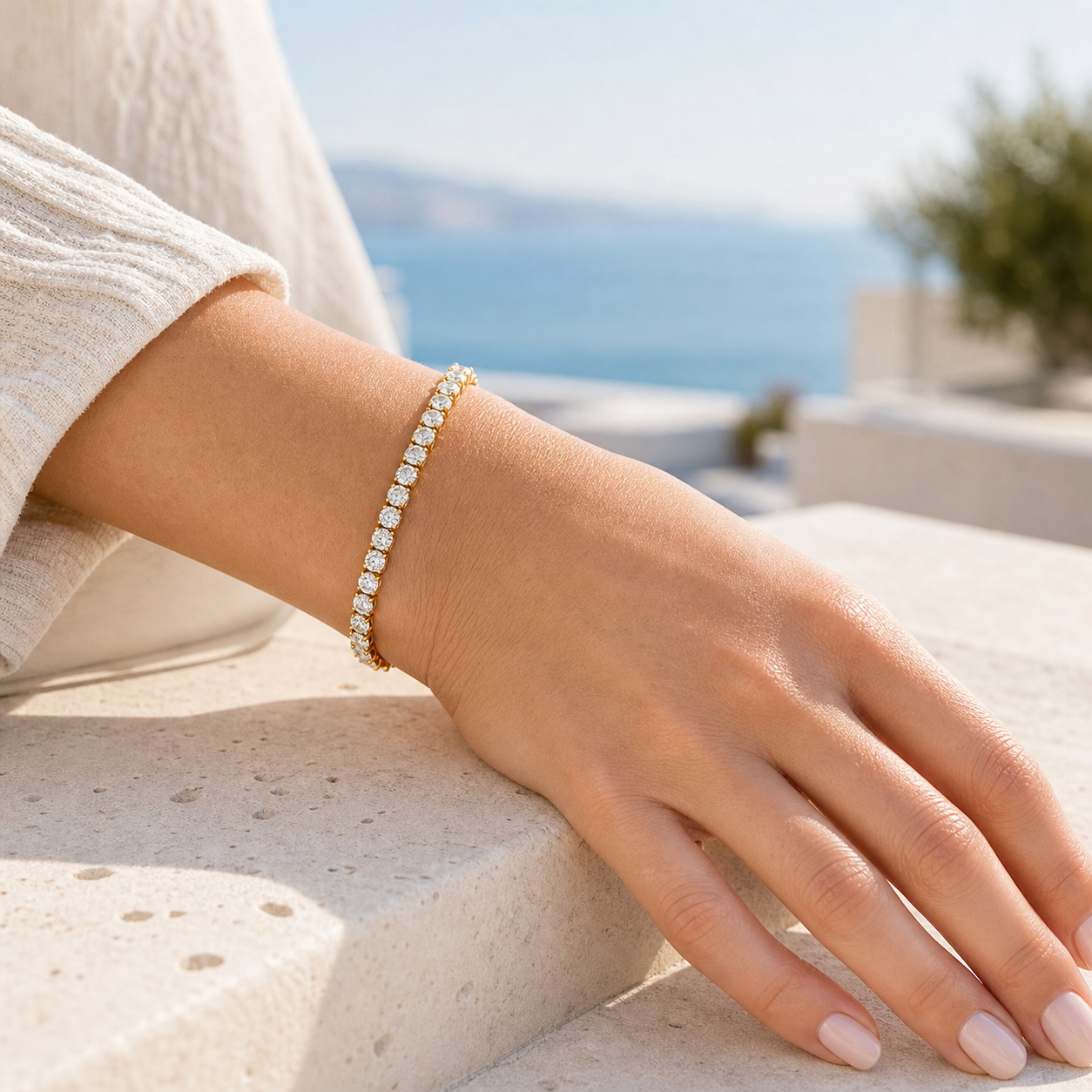 Brățară tennis aurie din oțel inoxidabil placat cu aur 18K PVD, cu zirconii, purtată pe o terasă luminoasă cu vedere la mare